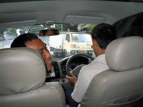 送迎車の車内で、助手席の日本語ガイドが後ろの旅行者に話しかけているところ