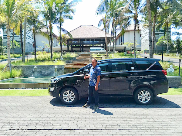ホテルの庭を背景に停まるカーチャーター車の横に立つドライバー
